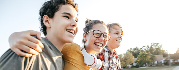 Three teenagers, one with headphones, walk and laugh together.
