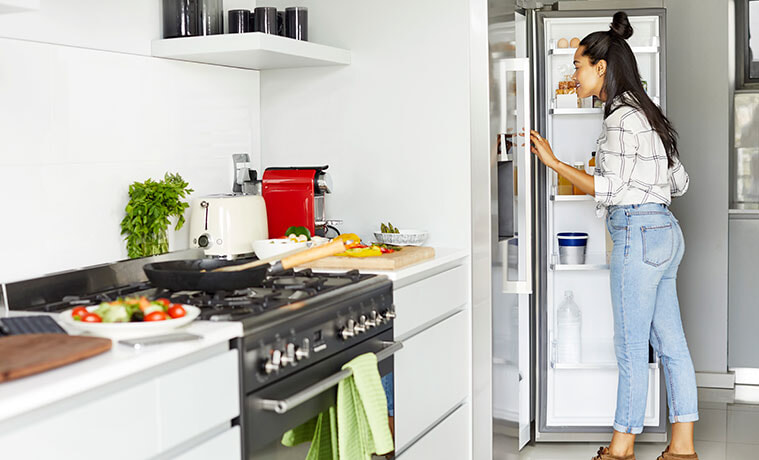 Woman searches for ingredients in her stainless steel fridge while cooking dinner.