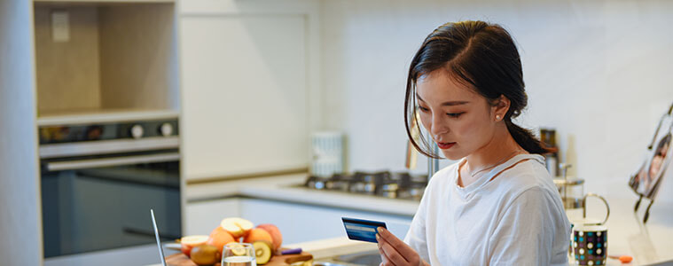 Young woman sitting at kitchen bench with laptop doing her finances.