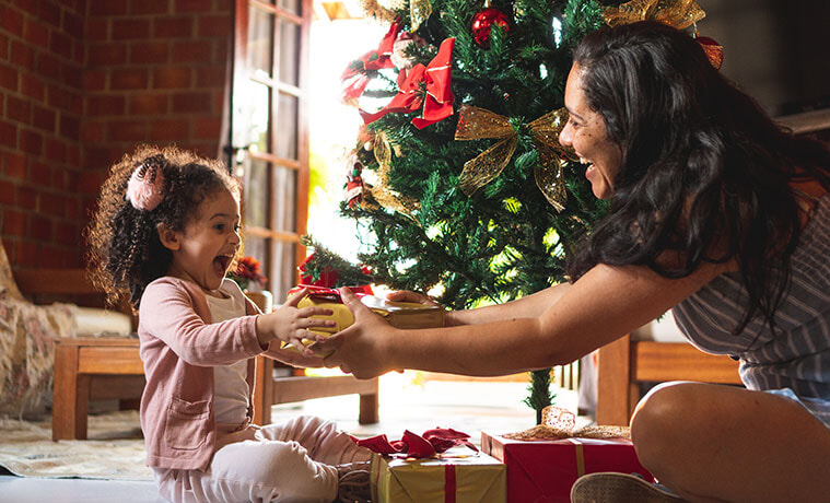 An excited young girl gives her mother a gift on Christmas morning. 