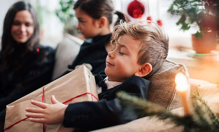 Smiling boy holding a Christmas present while sitting with family.