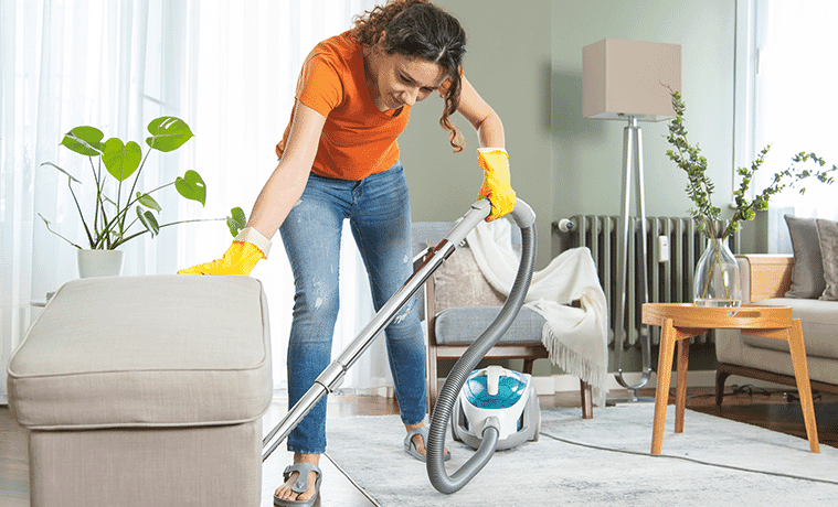 Woman moves an armchair to vacuum the rug in her living room.