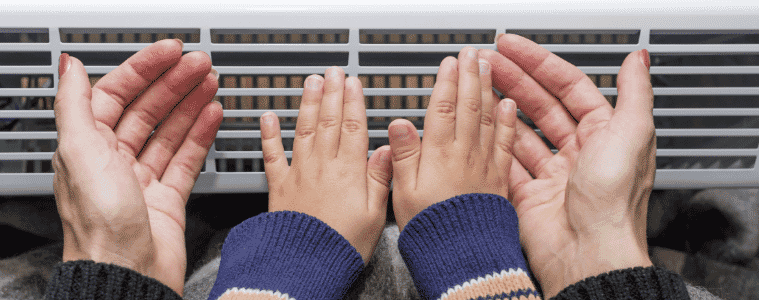 A mother and son warming up their hands next to an electric heater 