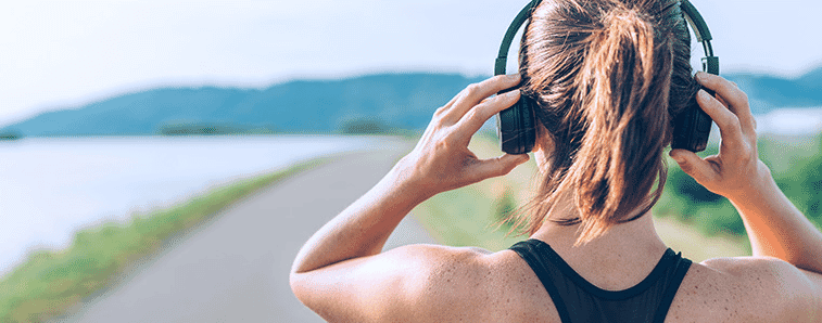 Happy female runner wears earphones while jogging in the morning in nature.