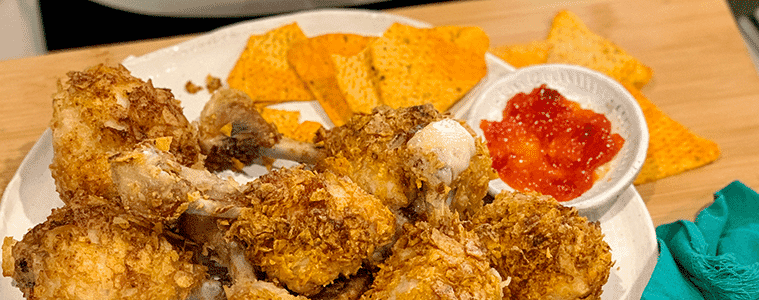 Air fryer chip crusted chicken drumsticks on a white plate with corn chips and potato chips . Image courtesy of Philips.