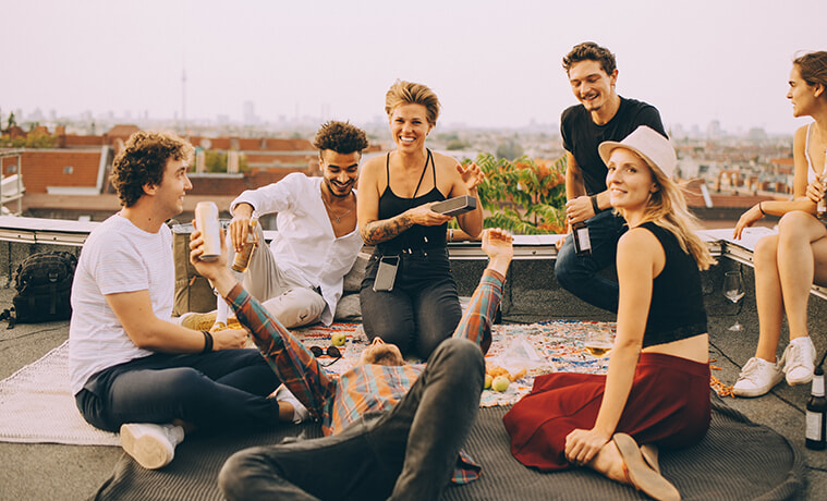 Friends enjoying music from an outdoor speaker during a rooftop party.