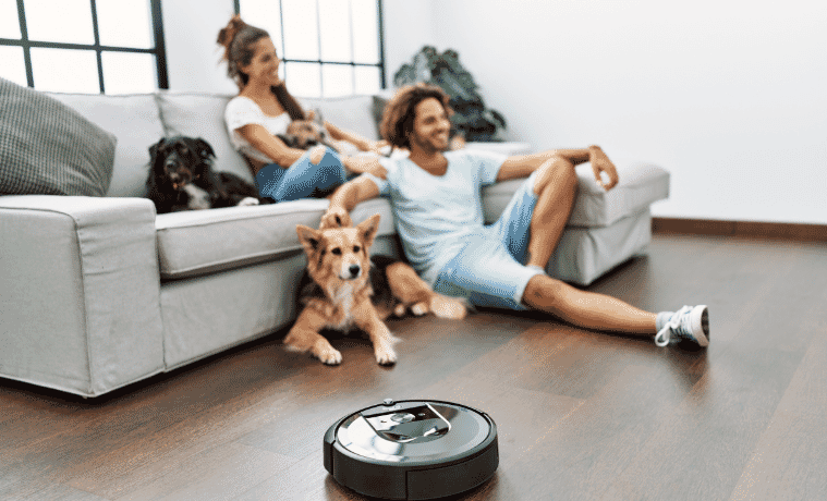A couple sitting on the couch with their dog while the robot vacuum cleans their floors 