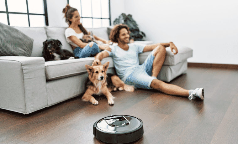 A couple sitting on the couch with their dog while the robot vacuum cleans their floors