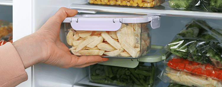 Close-up view of a woman taking a container of frozen potato chips from the fridge.
