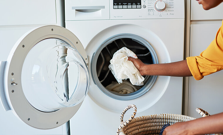 Close-up shot of a woman placing a white lace cloth into a front loading washing machine in her laundry