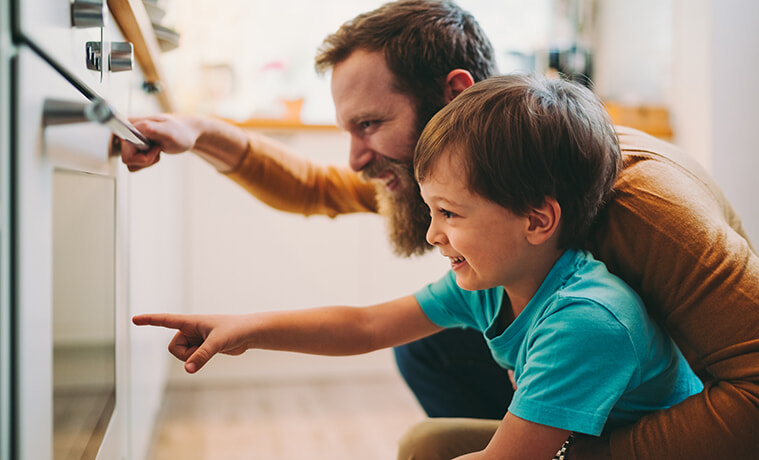 A father and his young son look through the oven door to see if dinner is ready.