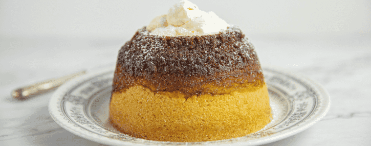 An individual treacle pudding, all buttery sponge cake and sticky golden syrup, served on a plate with a dollop of cream.