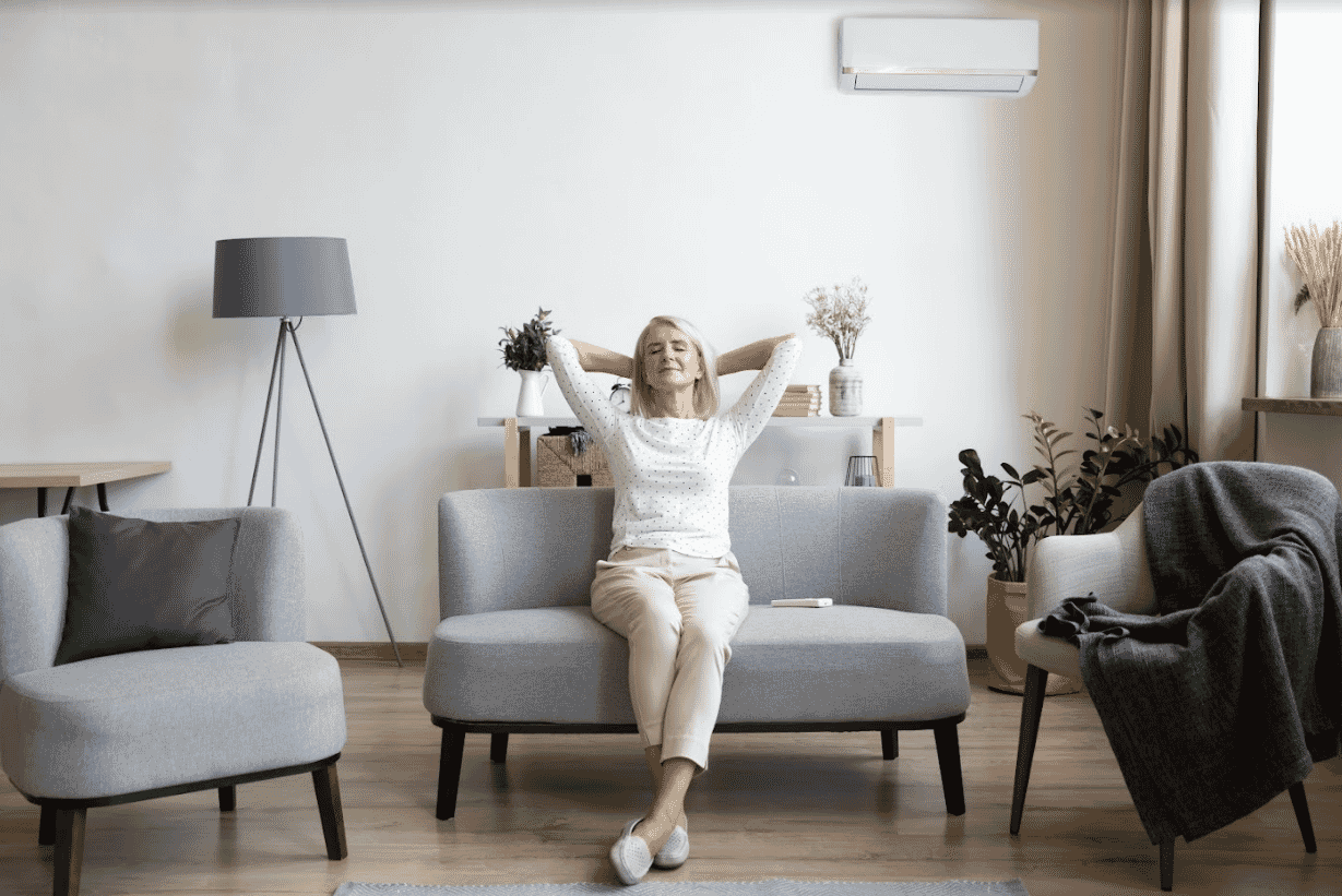 Relaxed woman sitting on a couch beneath a wall-mounted air conditioner. 