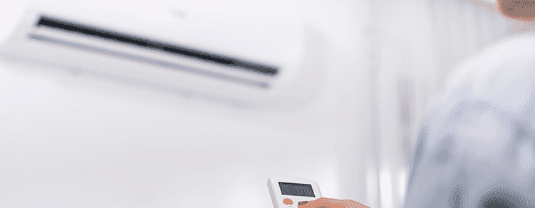 A woman holding the remote control for an air conditioner on a white wall.