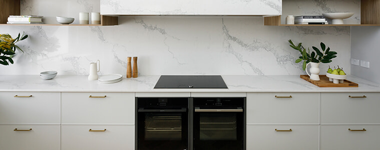White modern kitchen cabinetry with integrated oven and brass-coloured handles.