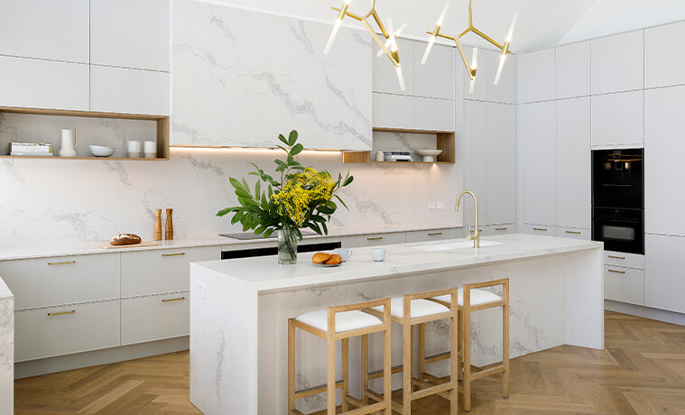 White coastal-style kitchen with marble-look island and herringbone floors.