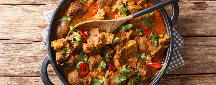 A pan of beef curry with red chilli and a wooden spoon.